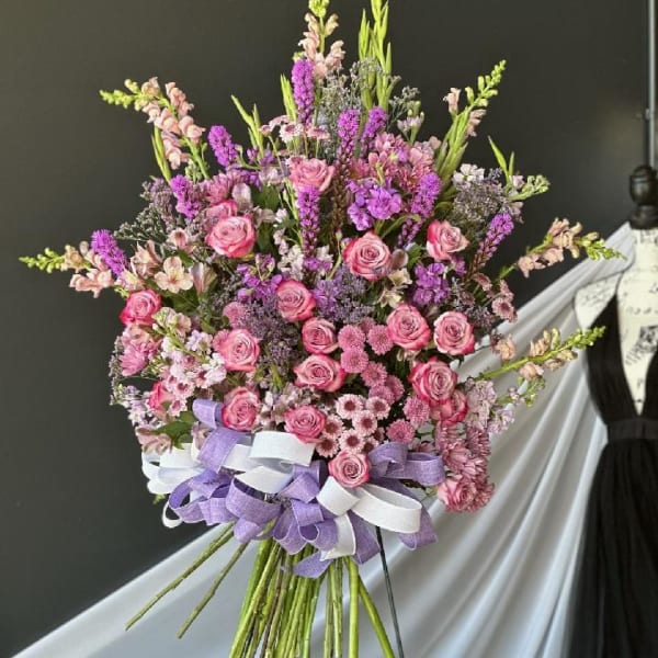 Large bouquet of pink and purple flowers tied with lavender and white ribbons