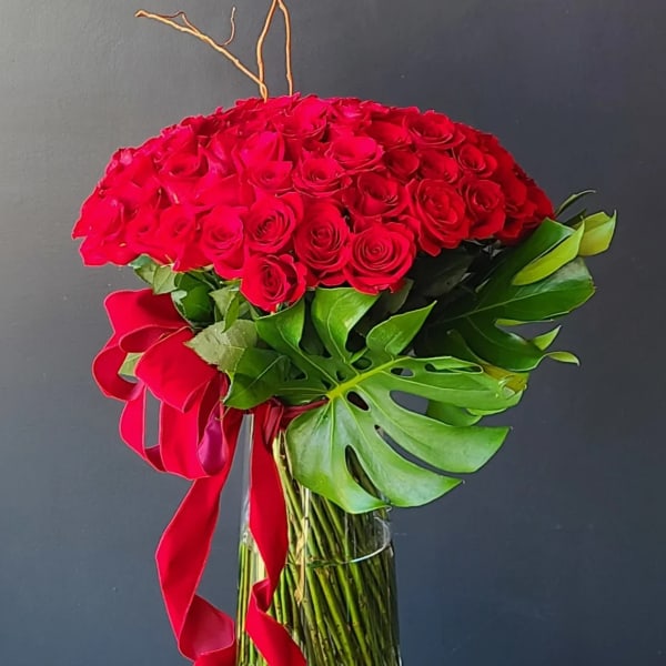 Red rose arrangement in a clear glass vase with a red ribbon