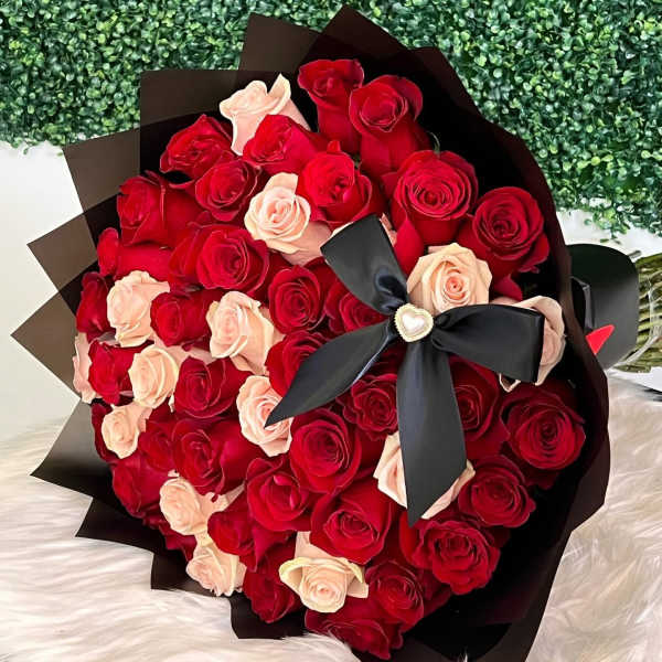 Large bouquet of red and blush roses wrapped in black paper with a black ribbon