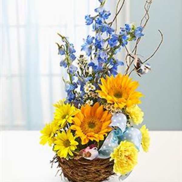 Yellow and blue flowers arranged in a wicker basket with ribbon