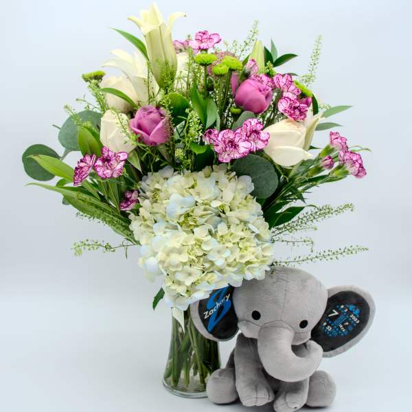 Bouquet of white and pink flowers in a glass vase with a gray plush elephant