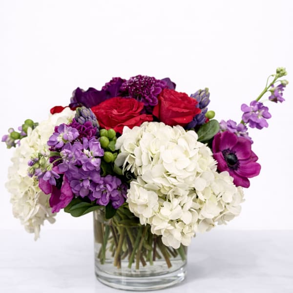Mixed bouquet of red, white, and purple flowers in a clear glass vase
