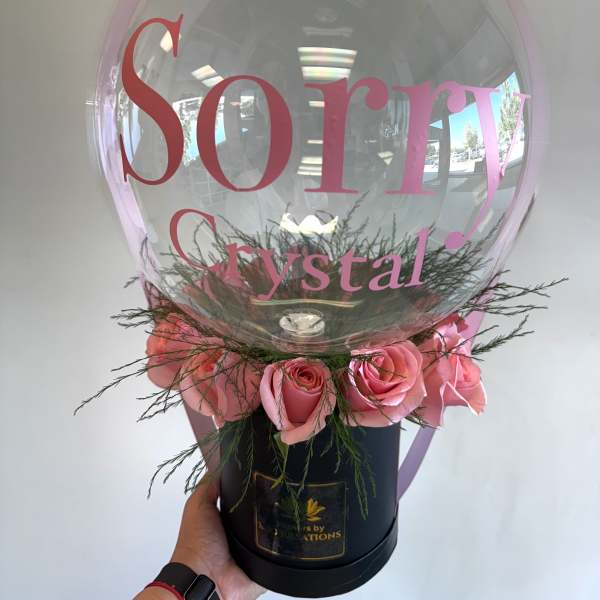 Pink roses arranged around a clear balloon with a pink bow