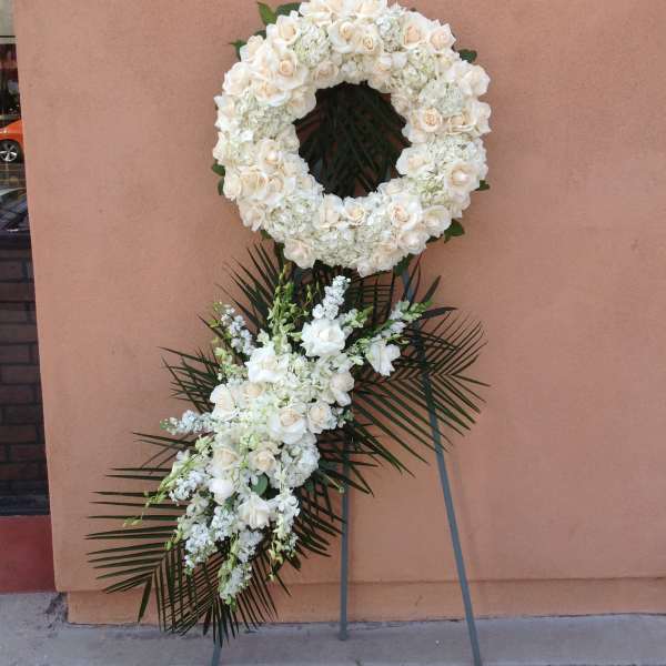 White floral wreath and spray on a stand with palm fronds