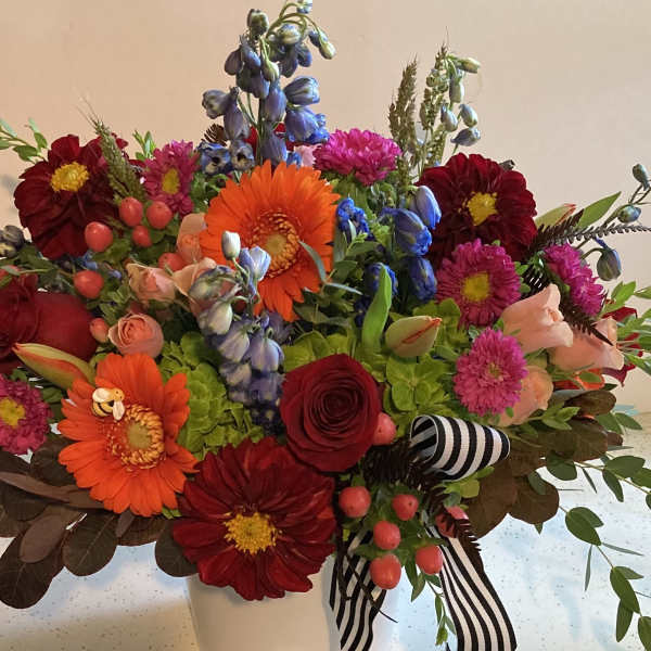 Mixed bouquet of bright flowers in a white vase with striped ribbon