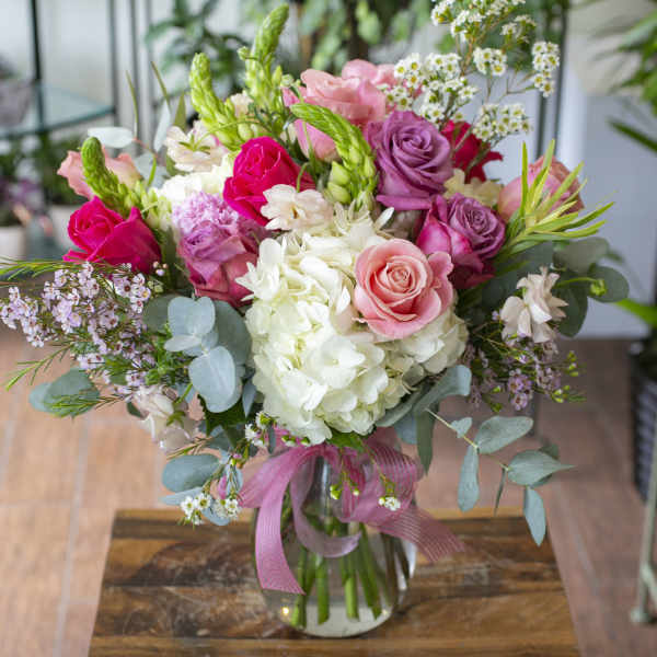 Pink and white rose bouquet in a glass vase with a ribbon