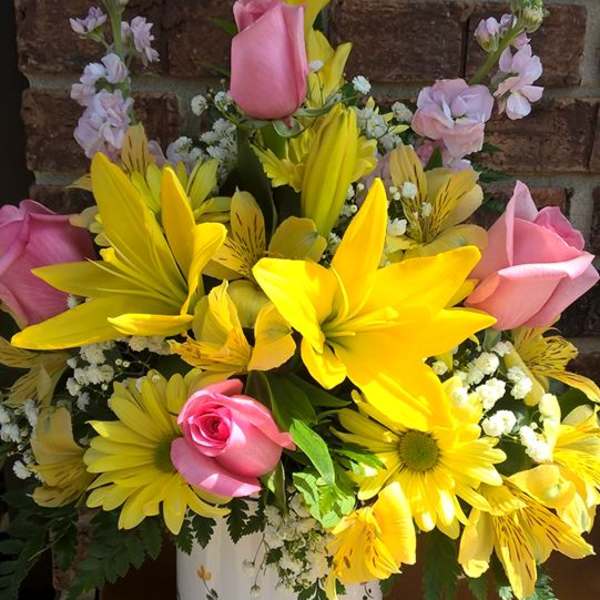 Yellow lilies and pink roses arranged in a white vase