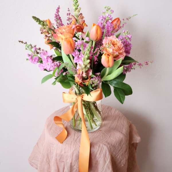 Orange and pink mixed bouquet in a clear glass vase with ribbon