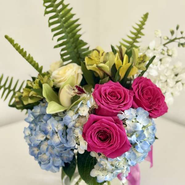Bouquet of pink roses, blue hydrangeas, and yellow lilies in a glass vase
