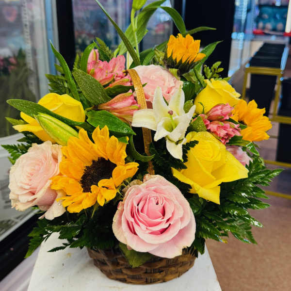 Basket arrangement of pink and yellow roses with sunflowers and white lilies