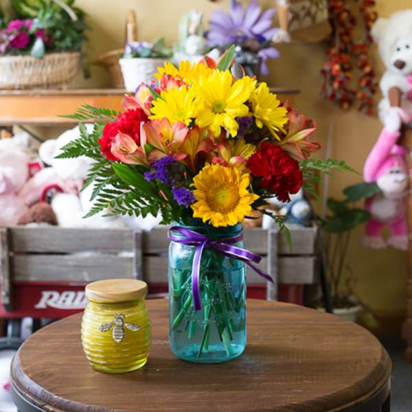 Bright mixed bouquet in a blue mason jar beside a small yellow candle jar