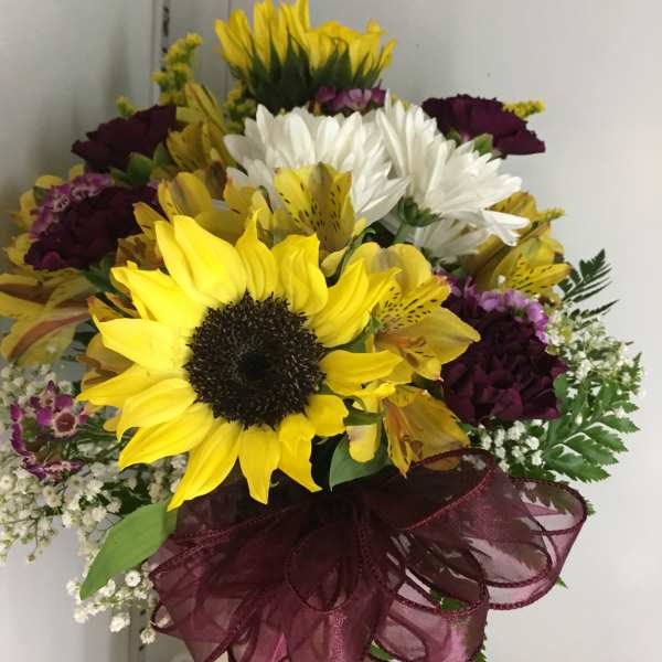 Bouquet of sunflowers, white daisies, and purple flowers with a burgundy ribbon