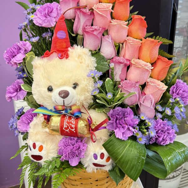Basket arrangement of pink and orange roses with a teddy bear holding candy