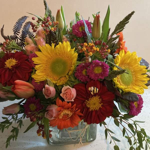 Mixed bouquet of sunflowers, roses, and gerbera daisies in a glass vase