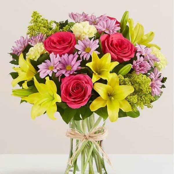 Bouquet of pink roses, yellow lilies, and lavender daisies in a glass vase