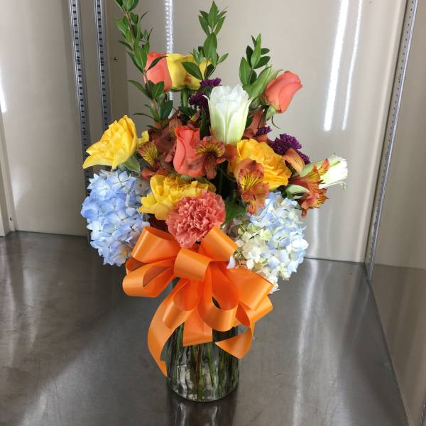 Colorful mixed flower arrangement in a glass vase with an orange bow