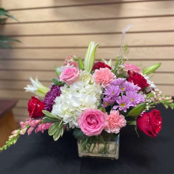 Mixed pink, white, and purple flower arrangement in a square glass vase