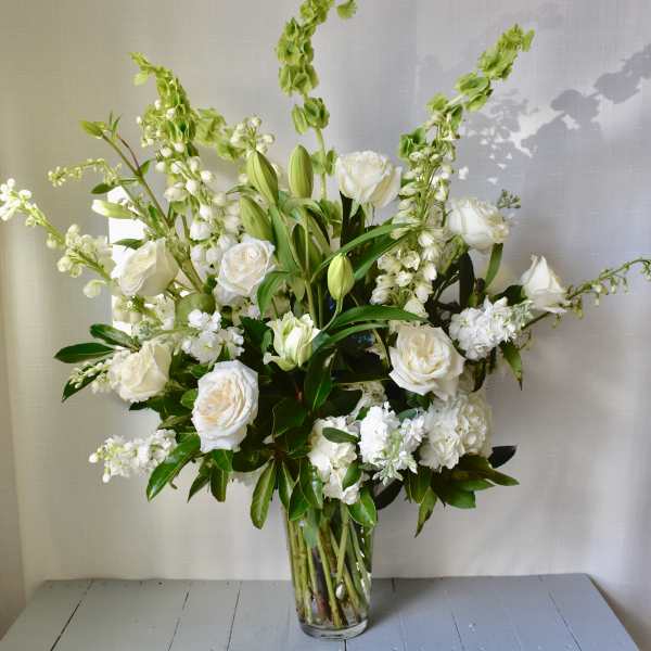 White floral arrangement in a clear glass vase with tall green spikes