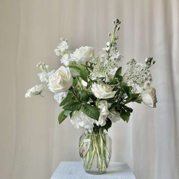 White roses and filler flowers in a clear glass vase