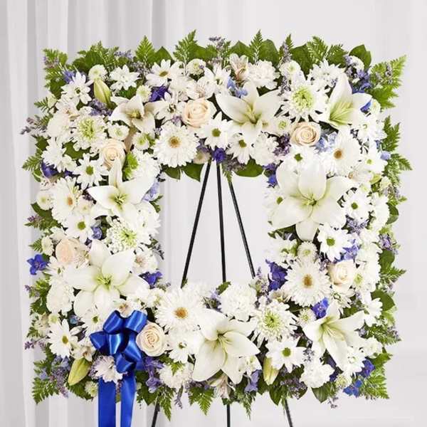 White floral standing wreath on an easel with a blue ribbon