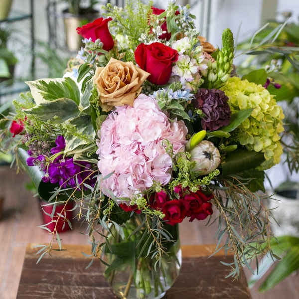 Mixed bouquet of roses, hydrangeas, and assorted blooms in a glass vase