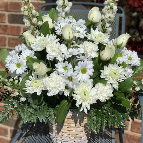White flowers arranged in a woven basket with green foliage