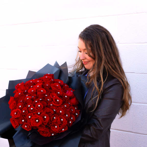 Woman holding a large bouquet of red roses wrapped in black paper