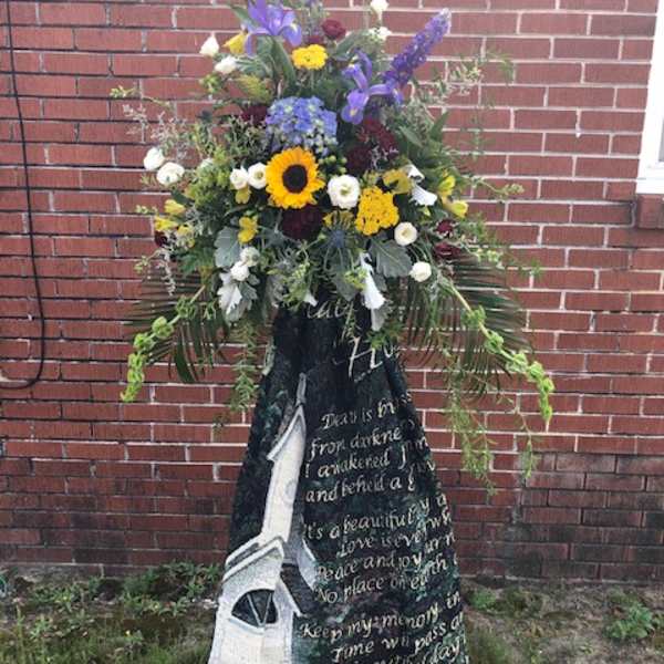 Standing funeral spray with mixed flowers and a memorial blanket drape