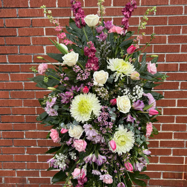 Tall standing spray of white, pink, and lavender flowers displayed on an easel.