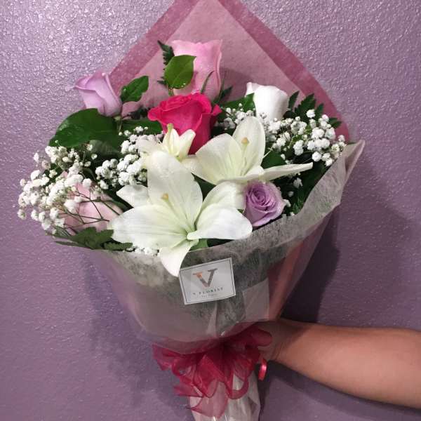 Wrapped bouquet of white lilies and mixed pink and purple roses held against a purple wall