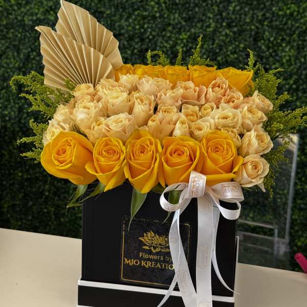 Yellow and cream roses arranged in a black box with a ribbon