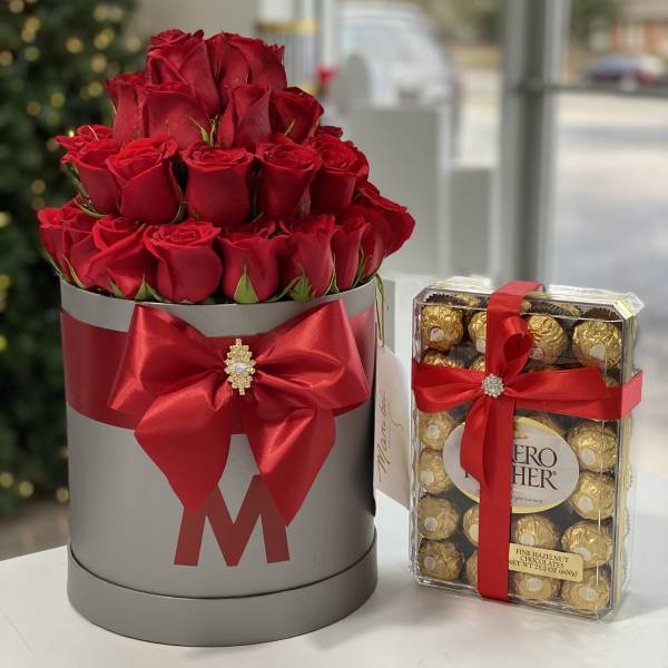 Red roses in a gray hatbox beside a box of chocolates tied with red ribbon