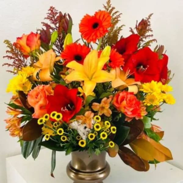 Bright mixed flower arrangement in a gold vase with red, orange, and yellow blooms