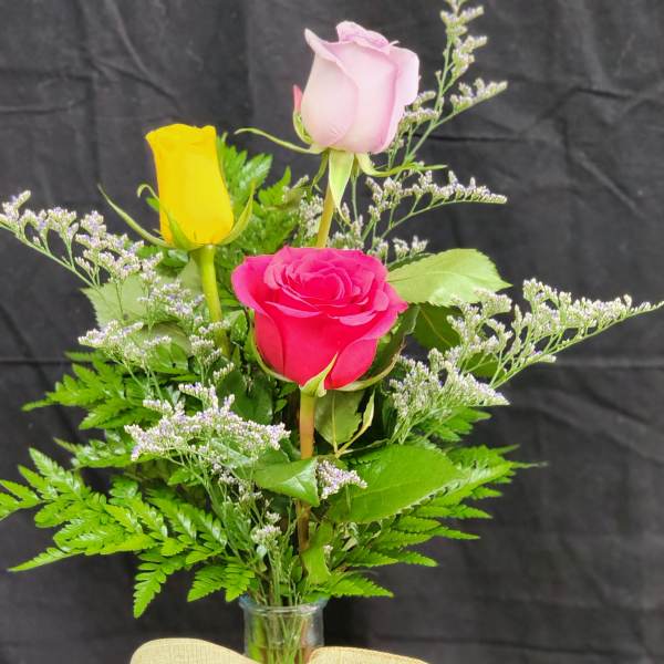 Three roses in a clear glass vase with a beige bow