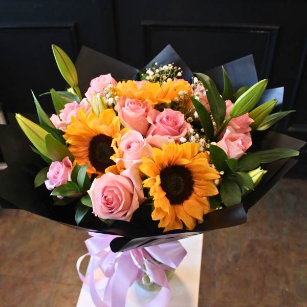 Bouquet of pink roses and sunflowers wrapped in black paper with a lavender ribbon