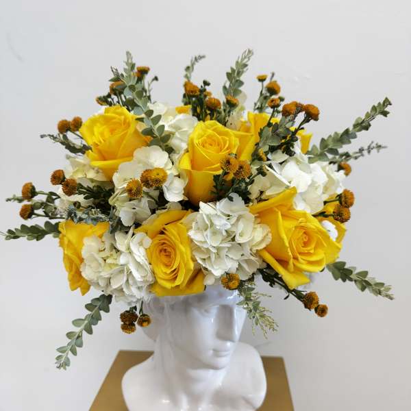 Yellow roses and white hydrangeas arranged in a white bust vase