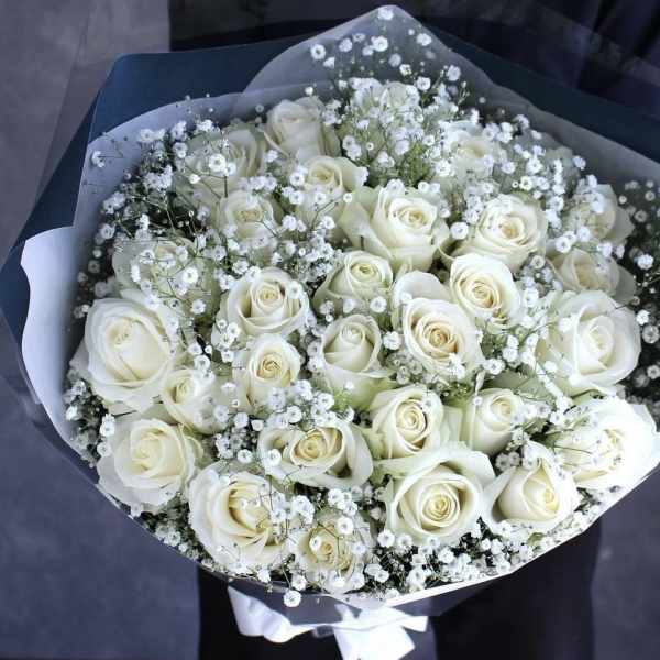 Bouquet of white roses and baby's breath wrapped in dark paper
