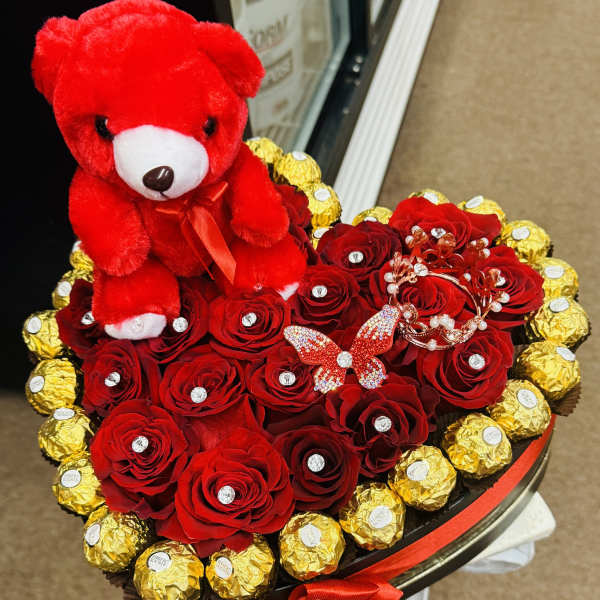 Heart-shaped bouquet of red roses with a red teddy bear and gold-wrapped chocolates