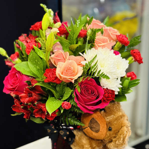 Bouquet of pink, peach, red, and white flowers with a teddy bear