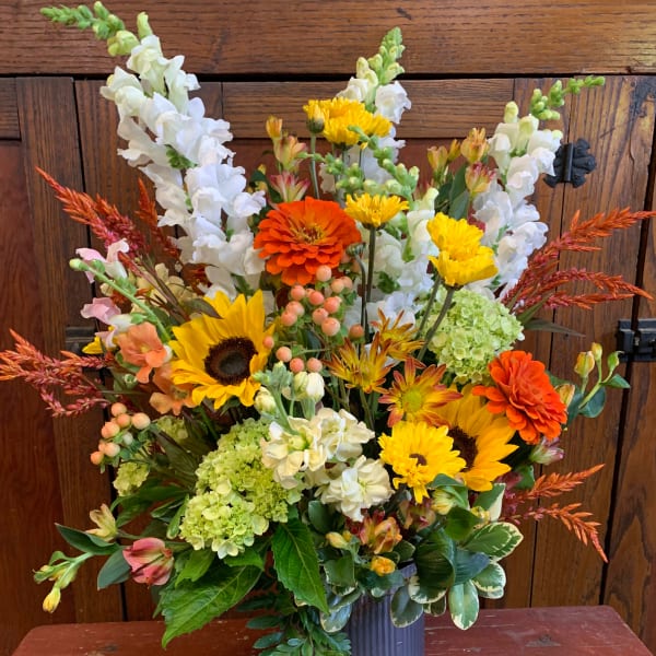 Mixed bouquet with sunflowers, orange zinnias, white snapdragons, and green hydrangeas in a metal vase