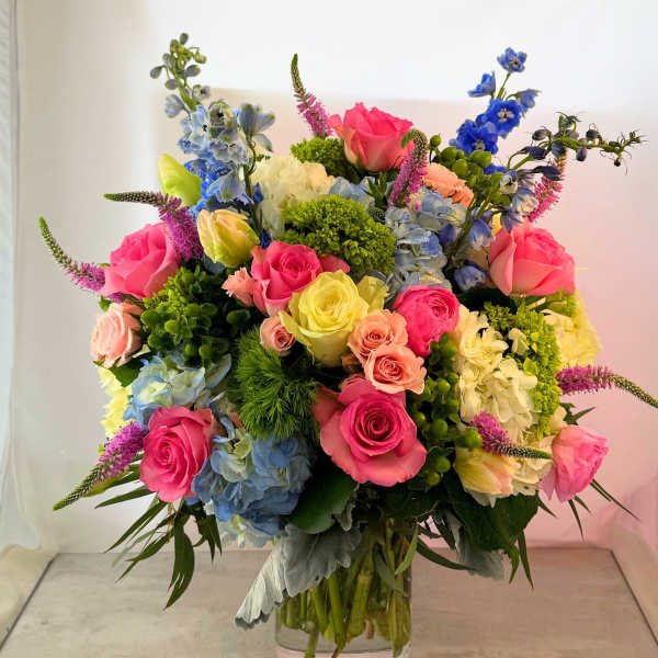 Colorful mixed bouquet in a clear glass vase with roses, hydrangeas, and blue flowers