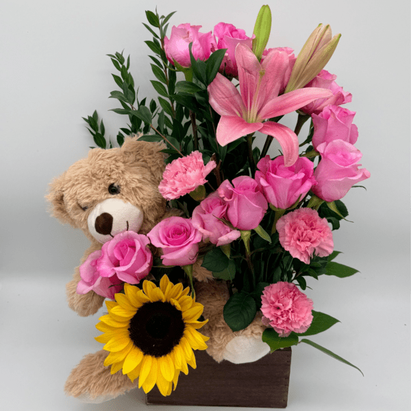 Pink roses and lilies arranged with a teddy bear and sunflower in a wooden box