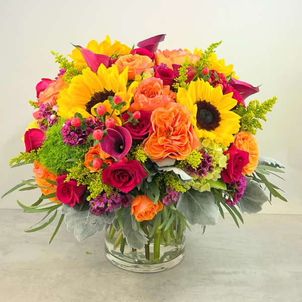 Bright mixed bouquet with sunflowers, roses, and calla lilies in a glass vase