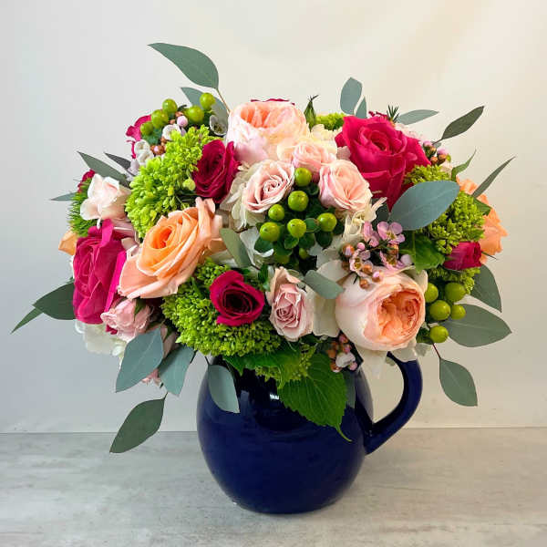 Mixed bouquet of pink, peach, and green flowers in a blue pitcher vase