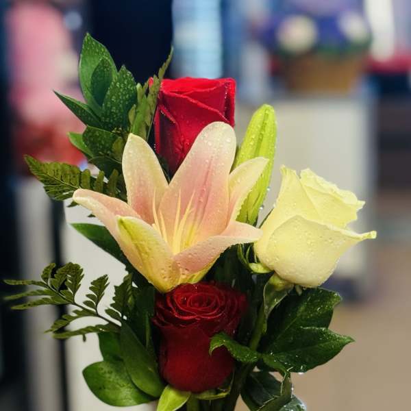 Bouquet of red roses and a pink lily in a glass vase with a red bow