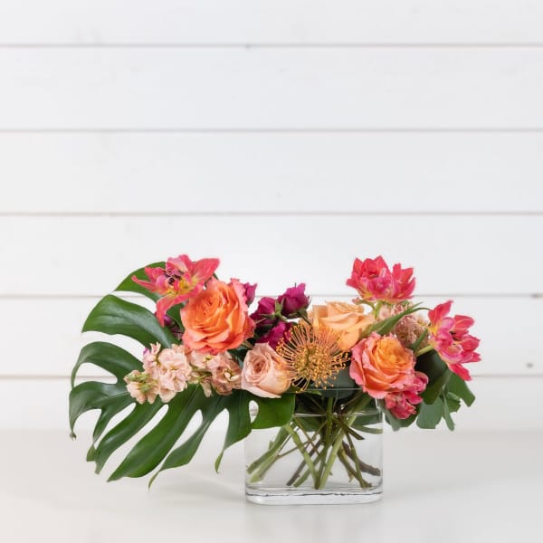 Mixed bouquet of orange and pink flowers in a clear glass vase