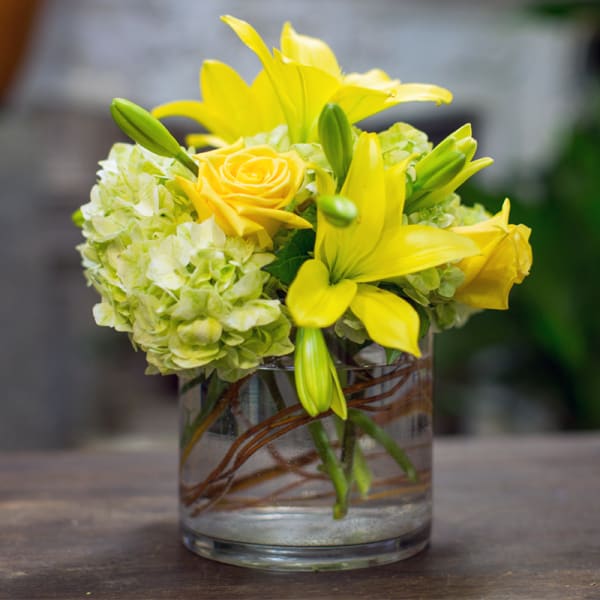 Yellow lilies and roses in a clear glass vase