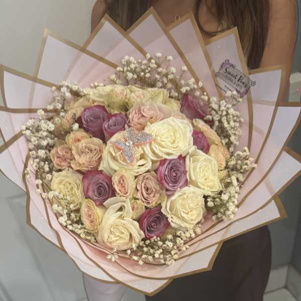 Handheld bouquet of cream, pink, and lavender roses wrapped in pink paper