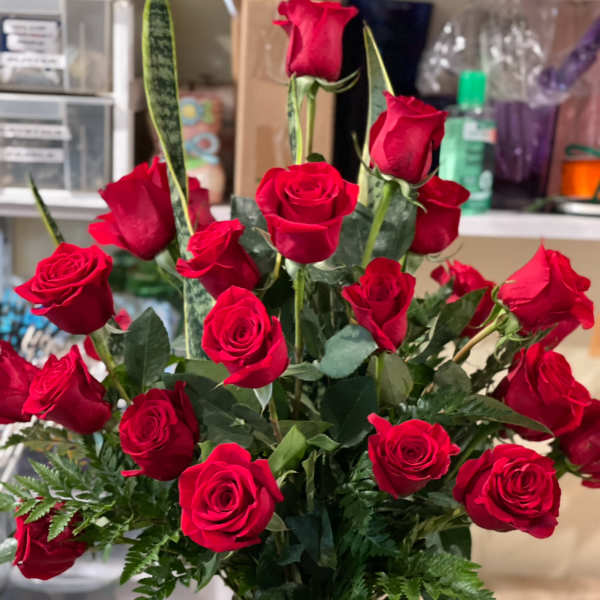 Tall bouquet of red roses in a clear vase with a red ribbon