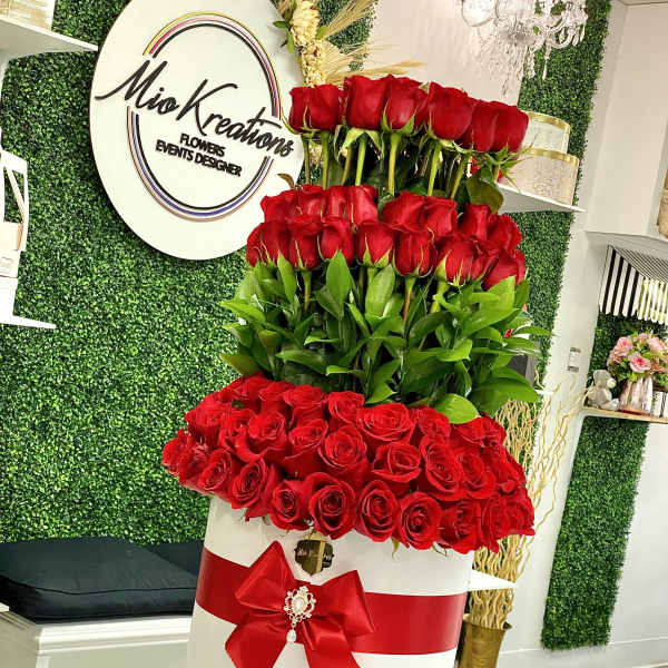 Tall tiered arrangement of red roses in a white box with a red bow